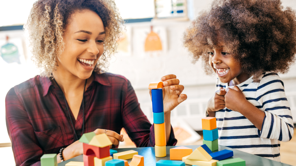 Dark skinned women smiling and helping a child with dark skin and curly hair build blocks. What can I do while on a waitlist for an autism assessment?