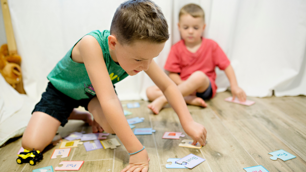 A young boy playing a puzzle on the floor. Another young boy is watching. Representing Autism and memory